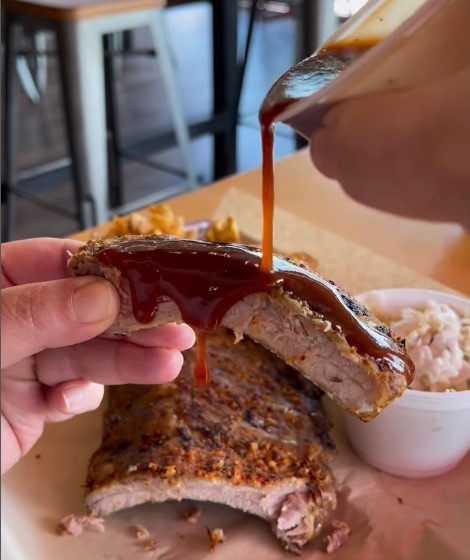 Barbecue sauce being poured over a cooked rib